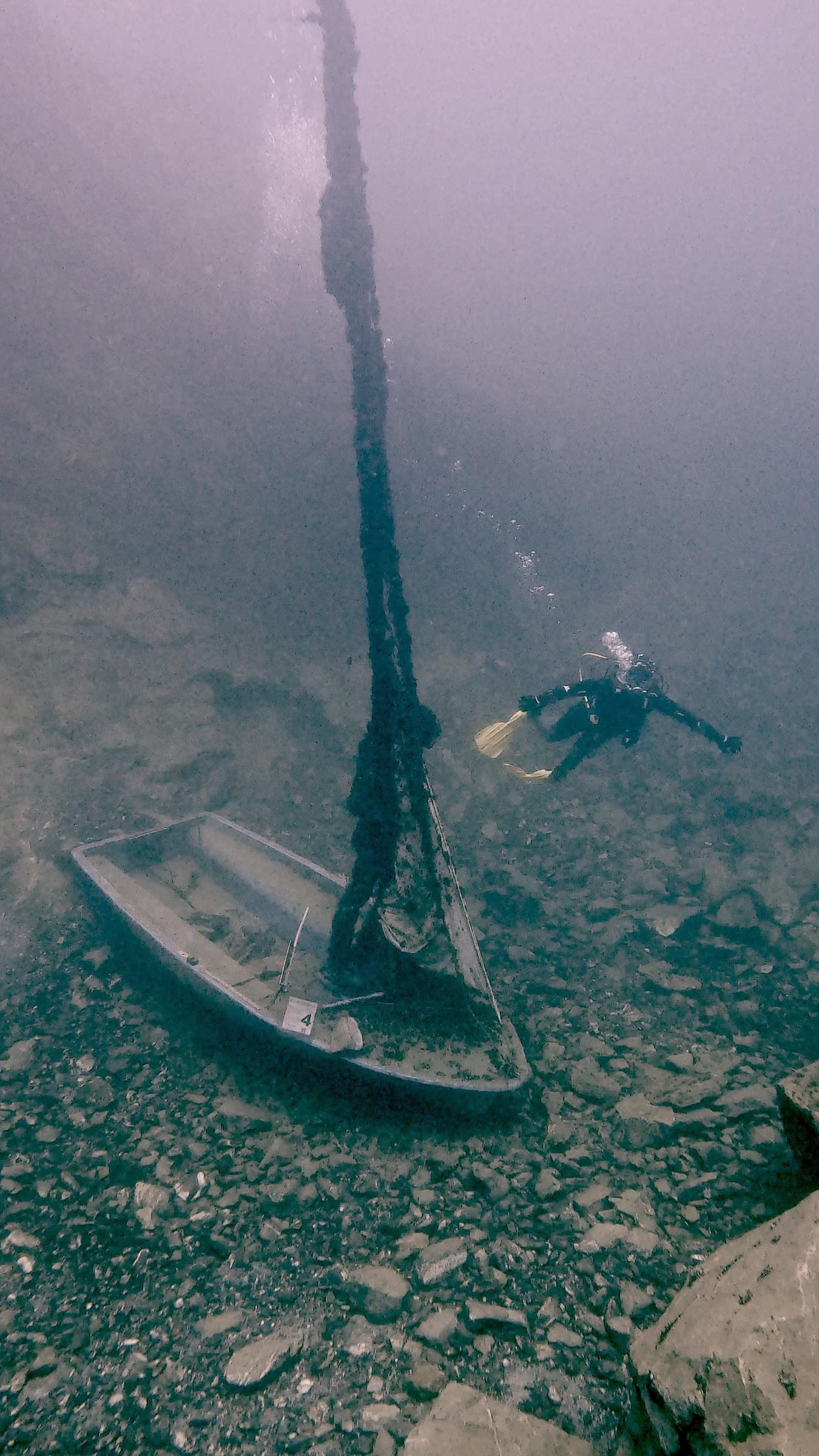Taucher schwebt über einem gesunkenen Segelboot auf dem Grund eines Sees
